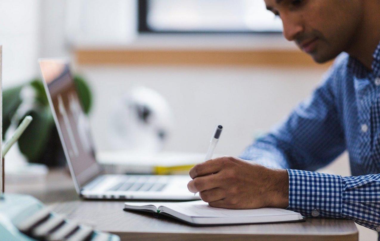 Man writes in a notebook next to a laptop